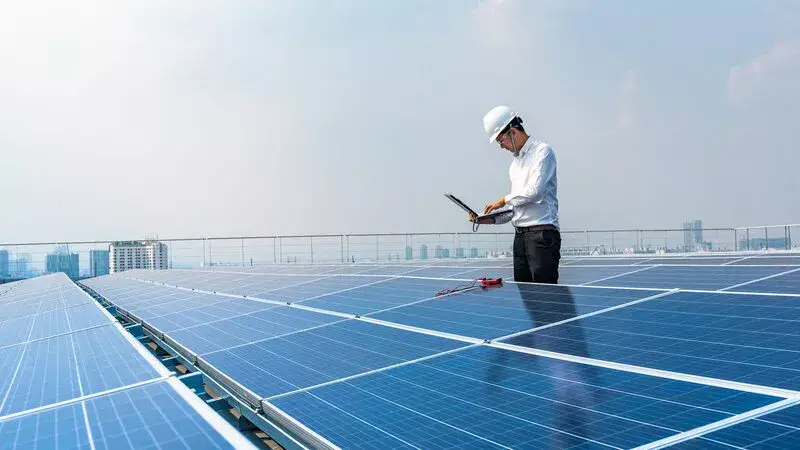 An energy engineer using a laptop standing in between solar panels.